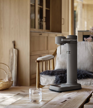 Kettle on a wooden table with a glass of water and aarke carbonator in a cozy room.