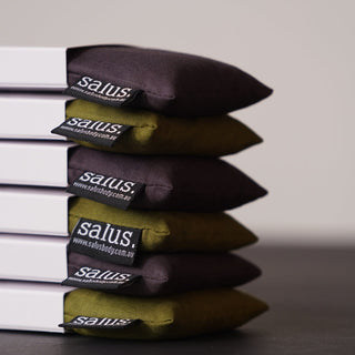 Stack of black and green pillows with 'salus' branding on a neutral background