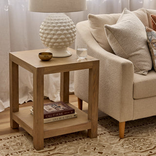 Wooden side table with decorative items next to a beige sofa in a living room setting.