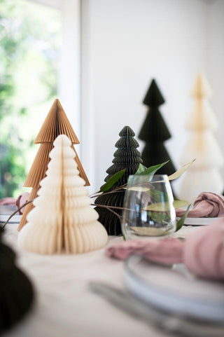 Decorative paper trees on a table with a glass and pink napkin.