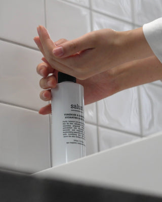 Person holding a white bottle labeled 'salus' against a tiled bathroom wall.