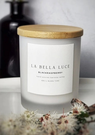 Candle with a wooden lid labeled 'La Bella Luce Blackraspberry' on a white surface.