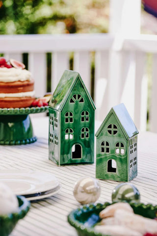 Two green ceramic house-shaped lanterns on a table with a blurred background