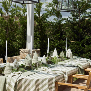 Outdoor dining table setting with decorative houses and striped tablecloth in a garden.