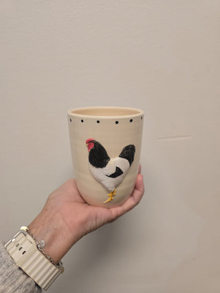 Hand holding a ceramic cup with a chicken design against a plain background