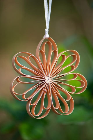 Decorative flower-shaped ornament made of paper or cardboard, hanging against a blurred natural background.