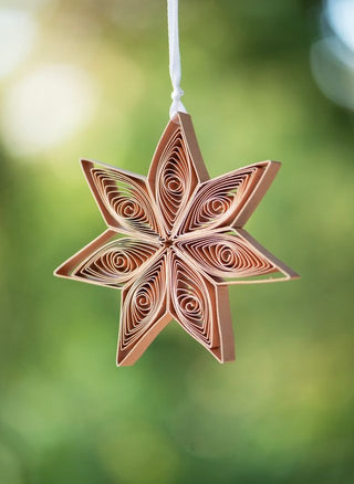 Decorative star ornament with a quilled design hanging against a blurred green background