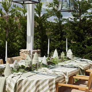 Outdoor dining table setting with decorative houses and striped tablecloth in a garden.