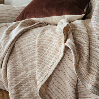 Textured beige blanket draped over a surface with a brown pillow in the background