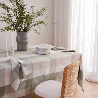 Dining table with a checkered tablecloth, plates, and a vase with greenery.