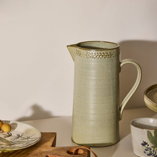 Green ceramic pitcher on a table with a neutral background