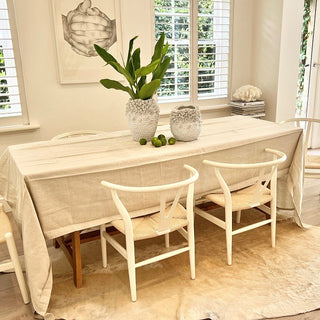 Dining room with a table covered in a beige cloth, two chairs, and decorative items.