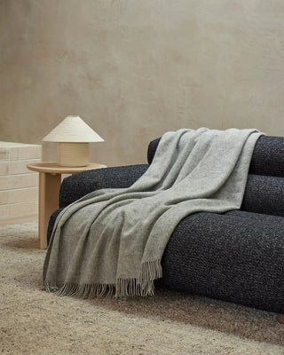 Gray blanket draped over a dark gray sofa with a wooden side table and lamp in the background.