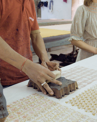 Person using a printing block on fabric with another person in the background.