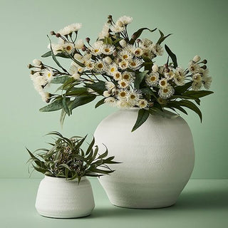 Two white ceramic vases with floral arrangements on a green background