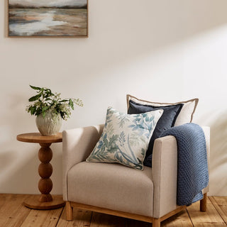 Beige armchair with decorative pillows and a wooden side table in a room.