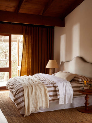 Cozy bedroom with wooden ceiling, bed with striped bedding, and lamp.