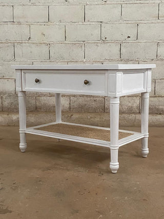 White wooden console table with a drawer against a brick wall.