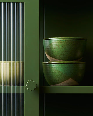 Green ceramic bowls stacked on a dark surface with a green cabinet in the background.