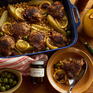 Baked chicken with lemon and olives in a blue baking dish on a wooden table.