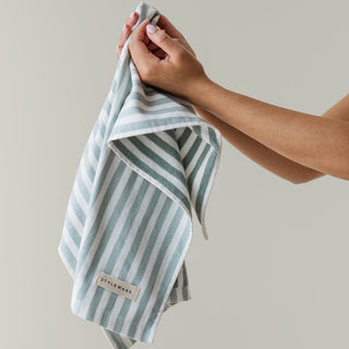 Hand holding a striped towel with a visible brand label against a neutral background