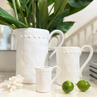 Set of white ceramic mugs with textured design on a surface with green limes and a plant.