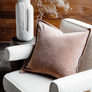Brown pillow on a textured chair with a decorative vase and branches in the background.