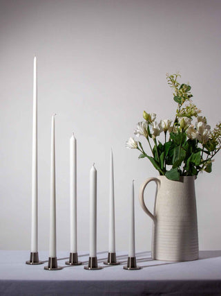 Set of white candles with metallic bases and a vase with flowers on a neutral background
