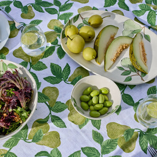 Table setting with a plate of sliced melon, pears, and a bowl of salad on a leaf-patterned tablecloth.