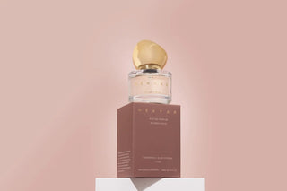 Perfume bottle with gold cap and brown box on a pink background