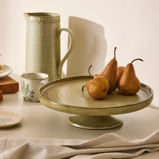 Ceramic pitcher, cup, and platter with pears on a neutral background