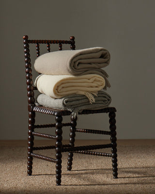 Stack of folded blankets on a wooden chair against a plain background