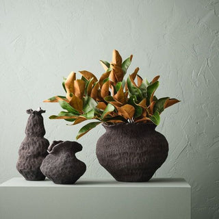 Decorative vase with plants and two small animal-shaped vases on a light surface against a textured light gray wall.