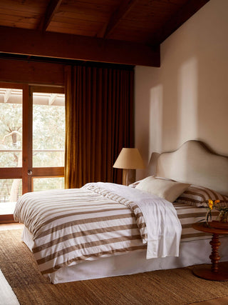 Bedroom with wooden ceiling and large windows, featuring a bed with striped bedding.