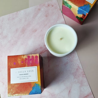 Candle in a white container with colorful packaging on a pink surface