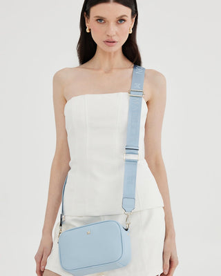 Woman wearing a light blue crossbody bag on a white background