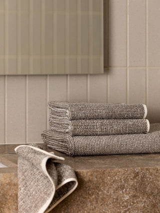 Stack of brown towels on a wooden surface with a tiled wall background