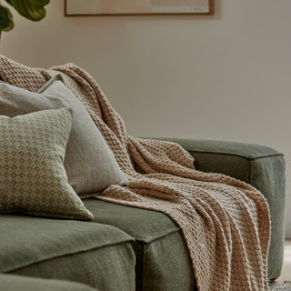 Green sofa with a brown blanket and pillows in a cozy living room.