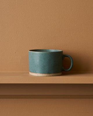 Blue ceramic mug on a brown shelf against a matching brown wall