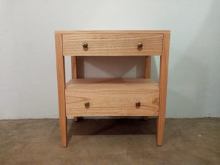 Wooden side table with two drawers against a plain wall.