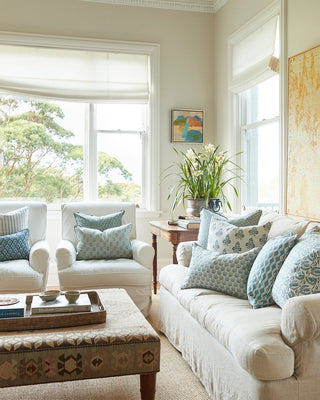 Living room with white sofa, armchair, and coffee table with decorative pillows and a plant.