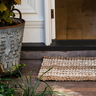 Doormat on a wooden floor with a plant and door in the background
