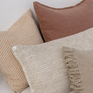 Three textured pillows in beige, brown, and another beige color on a light background.