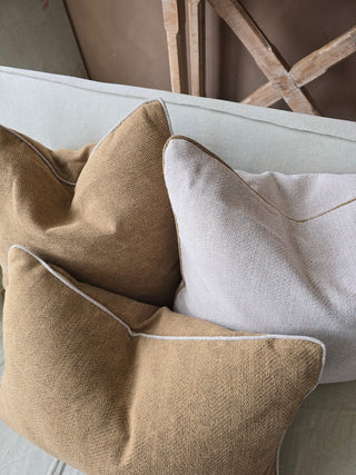 Two brown pillows and one white pillow on a light-colored surface with a blurred background.