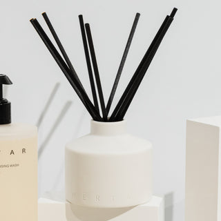 Reed diffuser with black sticks in a white container on a light background