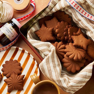 Box of gingerbread cookies with a cup of coffee and a bottle of syrup on a wooden table.