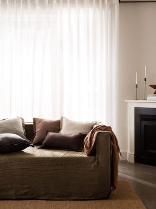 Brown sofa with cushions in a living room setting with a fireplace and large window.