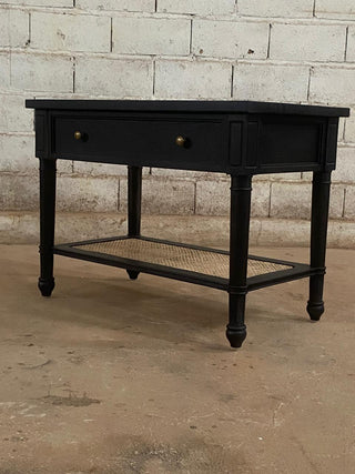 Black wooden console table with a single drawer against a brick wall.
