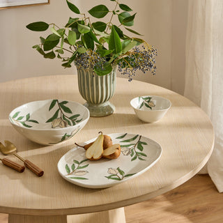 Dishes with floral patterns on a wooden table with a vase of greenery.