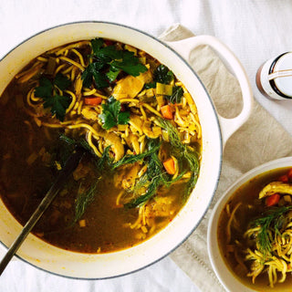 Noodle soup with vegetables in a white pot on a light background
